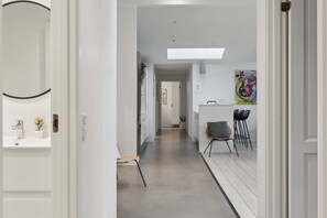 Un pasillo que conduce a un comedor de diseño moderno, con una pared blanca y una obra de arte colorida, y una silla con cojín.