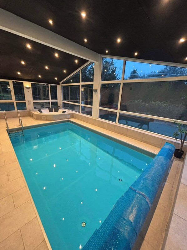 Ein rechteckiger, überdachter Pool mit klarem, blauem Wasser, umgeben von Fliesenböden und großen Fenstern.