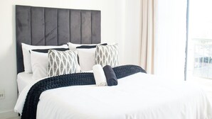 Una cama bien hecha con un cabecero gris, ropa de cama blanca y almohadas estampadas.