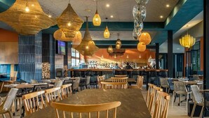 Un comedor amplio con varias mesas y sillas de madera, lámparas colgantes y una barra al fondo.