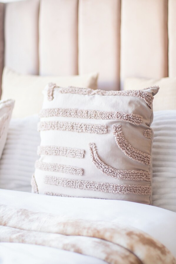 A bed with a beige upholstered headboard and a decorative pillow with tassels.