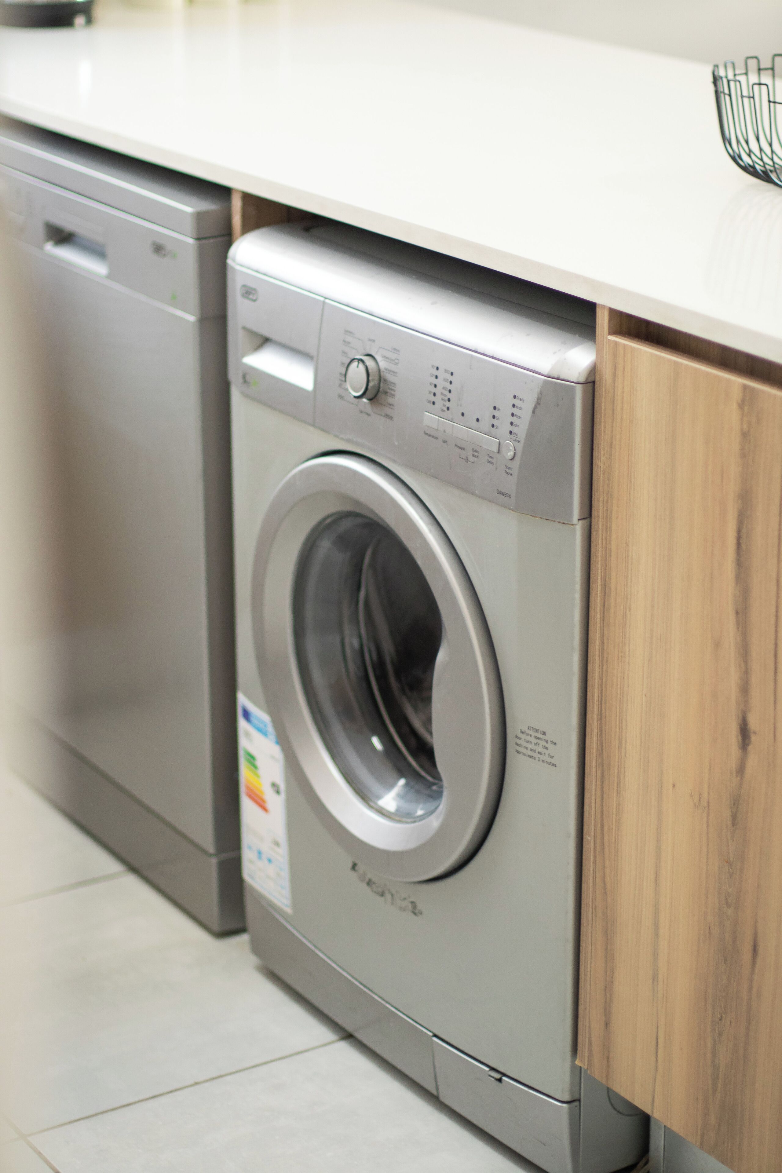 Een voorlader wasmachine in een keuken met een houten kast en een witte aanrechtblad.