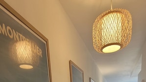 A hallway with a large framed picture of a building, a hanging light fixture, and a view into a dining area. - Cosy apartment large T1 of 32m2, direct access to the beach (Mauguio)