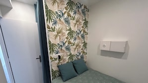 A small, neatly arranged bedroom with a bed, two pillows, a wall-mounted power outlet, and a white cabinet. - Cosy apartment large T1 of 32m2, direct access to the beach (Mauguio)