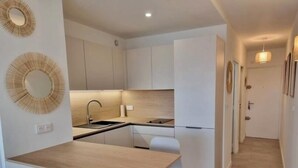 A compact kitchen with a central island, white cabinetry, and a small dining area. - Cosy apartment large T1 of 32m2, direct access to the beach (Mauguio)