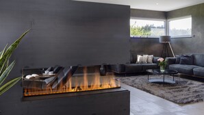 A modern living room with a glass-top fireplace, a black leather sofa, a coffee table, and a large window. - Apartment 'Riedheide, 130qm' with Private Terrace, Private Garden and Wi-Fi (Bad Wurzach)