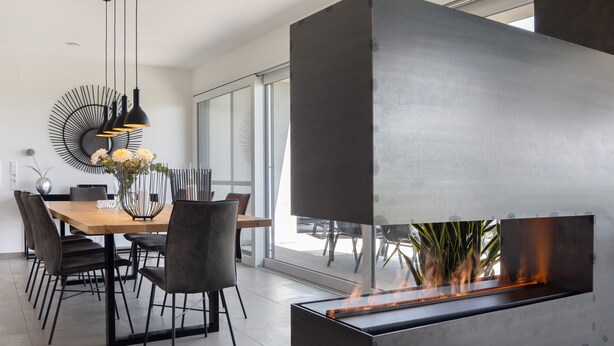 A modern dining area with a long table, chairs, pendant lights, and a built-in fireplace. - Apartment 'Riedheide, 130qm' with Private Terrace, Private Garden and Wi-Fi (Bad Wurzach)
