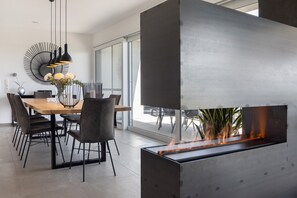 A modern dining area with a long table, chairs, pendant lights, and a built-in fireplace. - Apartment 'Riedheide, 130qm' with Private Terrace, Private Garden and Wi-Fi (Bad Wurzach)