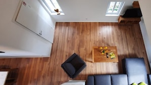 A room with a wooden floor, a sofa, a coffee table with flowers, and a window. - Apartment 'Kornkammer' with Shared Garden, Balcony and Wi-Fi (Finnentrop)