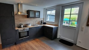 A modern kitchen with dark cabinets, a stainless steel range hood, a kettle, a coffee maker, and a window providing a view of the outdoors. - Apartment 'Kornkammer' with Shared Garden, Balcony and Wi-Fi (Finnentrop)