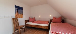 Un dormitorio con dos camas, una silla de madera y un cuadro en la pared.