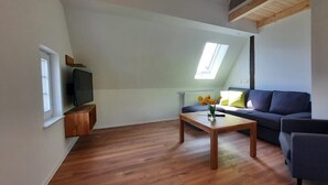 A modern living room with a dark sofa, a wooden coffee table, and a television on a stand. - Apartment 'Kornkammer' with Shared Garden, Balcony and Wi-Fi (Finnentrop)