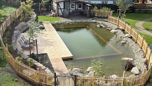A circular pond with a wooden deck, surrounded by a wooden fence, and a small building with a sloped roof. - Apartment 'Kornkammer' with Shared Garden, Balcony and Wi-Fi (Finnentrop)