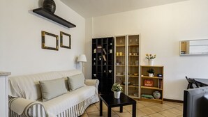 A living room with a sofa, a coffee table, a bookshelf, and a television. - GuestHost - Naviglio Pavese Comfortable Apt with Balcony! (Milano)