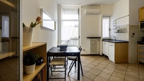 A compact kitchen with a dining table, chairs, a radiator, and a window with sheer curtains. - GuestHost - Naviglio Pavese Comfortable Apt with Balcony! (Milano)