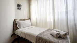 A neatly made bed with a quilt, pillows, and a rolled towel, a wall-mounted picture, and sheer curtains. - GuestHost - Naviglio Pavese Comfortable Apt with Balcony! (Milano)