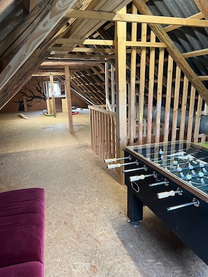 Une chambre mansardée avec un plafond en bois, une table de baby-foot et un fauteuil violet.