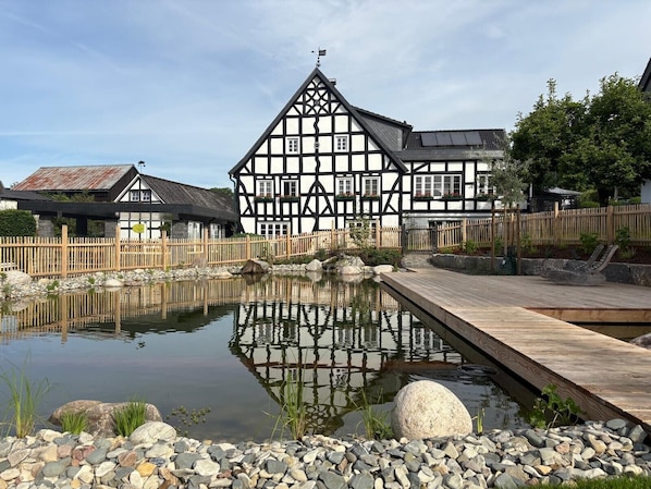 Un bĂątiment traditionnel Ă colombages, dotĂ© dâun Ă©tang et dâune terrasse en bois.