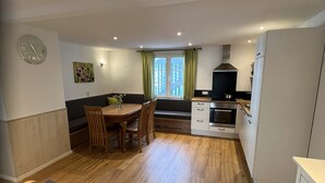 Une cuisine compacte avec un coin repas, un four encastré et une fenêtre avec des rideaux.
