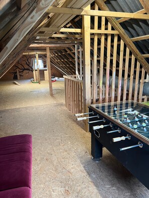 Une chambre mansardée avec un plafond en bois, une table de baby-foot et un fauteuil violet.