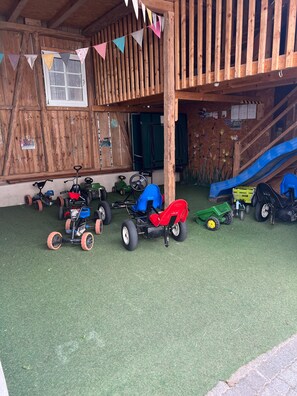 Eine Holzkonstruktion mit einer Rutsche, Kindertricycles und einem grünen Traktor.