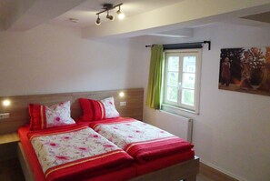 A double bed with a floral bedspread, a headboard, a window with a curtain, and a wall-mounted light fixture. - Apartment 'Apfelbaum' with Private Terrace, Shared Garden and Wi-Fi (Finnentrop)