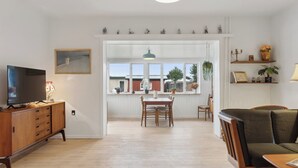 Una sala de estar con un aparador de madera, televisor, mesa de comedor con sillas, sofá y ventana con vistas al exterior.