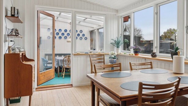Un comedor con mesa y sillas de madera, una cocina con armarios blancos, y vistas a través de un ventanal.