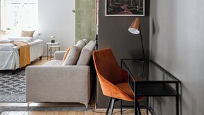 A modern living room with a bed, a sofa, a chair, a table, and a painting on the wall.