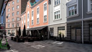 A public square with a green electric scooter, outdoor seating, and a variety of shops and restaurants.