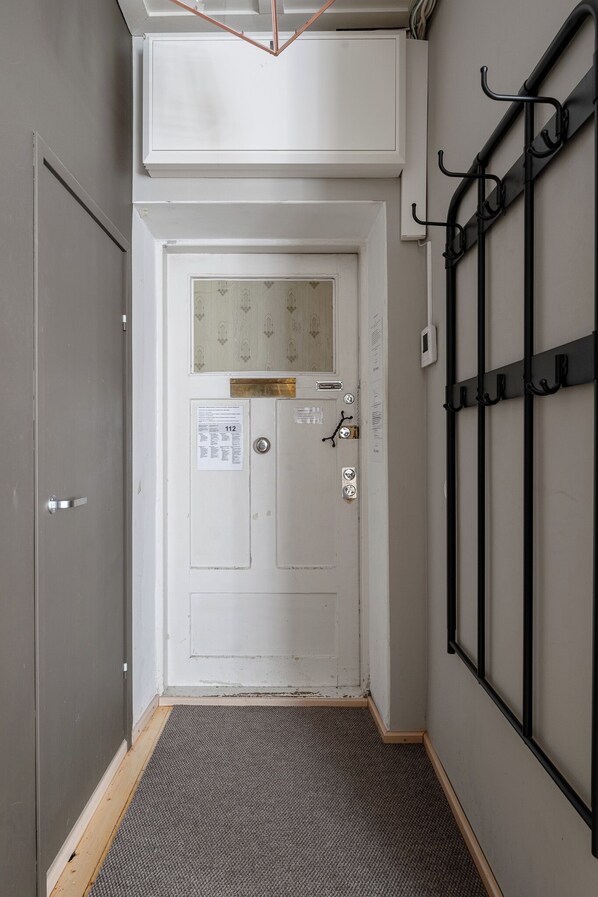 Un pasillo estrecho con una puerta blanca, un perchero de metal y un felpudo en la entrada.