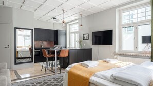 A modern hotel room with a bed, a desk, a chair, a TV, and a kitchen area.