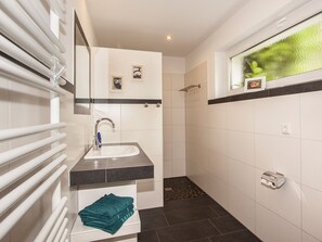 Une salle de bain moderne équipée d’un lavabo, d’un miroir, d’un porte-serviettes et d’un espace douche.