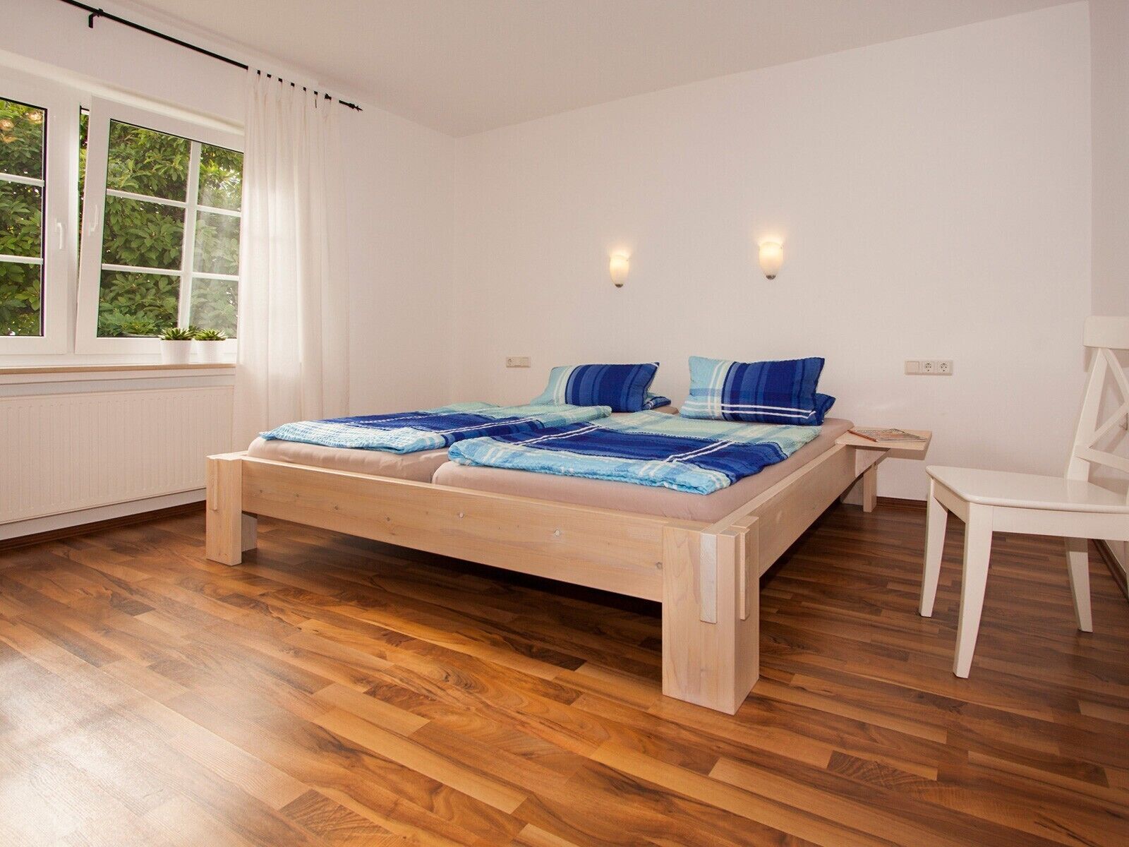 Une chambre à coucher avec un lit en bois, une chaise blanche et une fenêtre avec des rideaux.