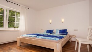 A bedroom with a wooden bed, a white chair, and a window with curtains. - Apartment 'Sonnenblume' with Private Terrace, Shared Garden and Wi-Fi (Finnentrop)