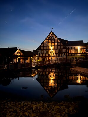 Un bâtiment traditionnel à colombages se reflétant dans l’eau, un ciel dégagé et une atmosphère paisible au crépuscule.