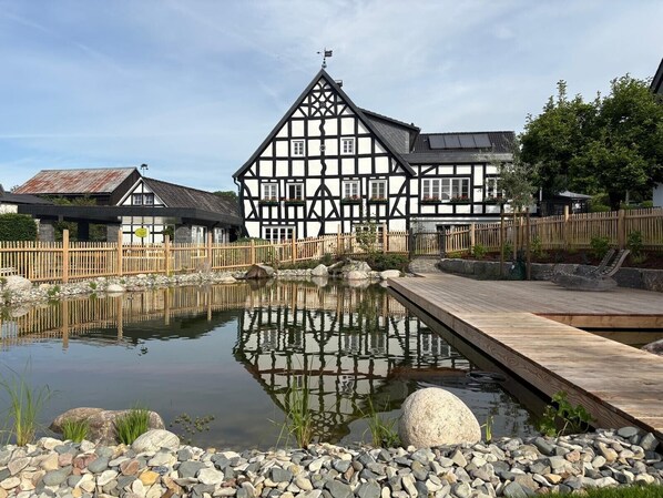 Un bâtiment traditionnel à colombages, doté d’un étang et d’une terrasse en bois.