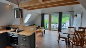 Ett modernt kök med ett takfönster, en matplats med möbler i trä och utsikt över en grön trädgård genom stora fönster.