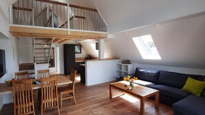 En lägenhet i loftstil med ett matområde, kök och ett vardagsrum med en soffa och ett fönster.