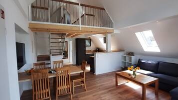 A loft-style apartment with a dining area, kitchen, and a living room with a sofa and a window.