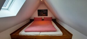 A small, triangular attic bedroom with a bed, pillows, and a painting on the wall. - Apartment 'Heuboden' with Shared Garden, Balcony and Wi-Fi (Finnentrop)