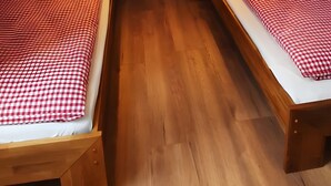 Ett litet, triangulärt sovrum på vinden med två sängar i trä, en taklampa och en tavla som hänger på väggen.