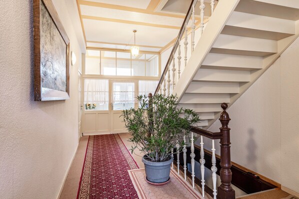 Una escalera con balaustres blancos y una alfombra roja que conduce a una habitación con un ventanal grande y una planta en maceta.