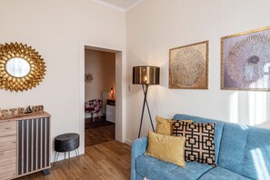 A room with a blue sofa, a wooden cabinet, a floor lamp, and wall art. - Holiday Apartment 'Seestern' with Shared Garden and Wi-Fi (Kühlungsborn)