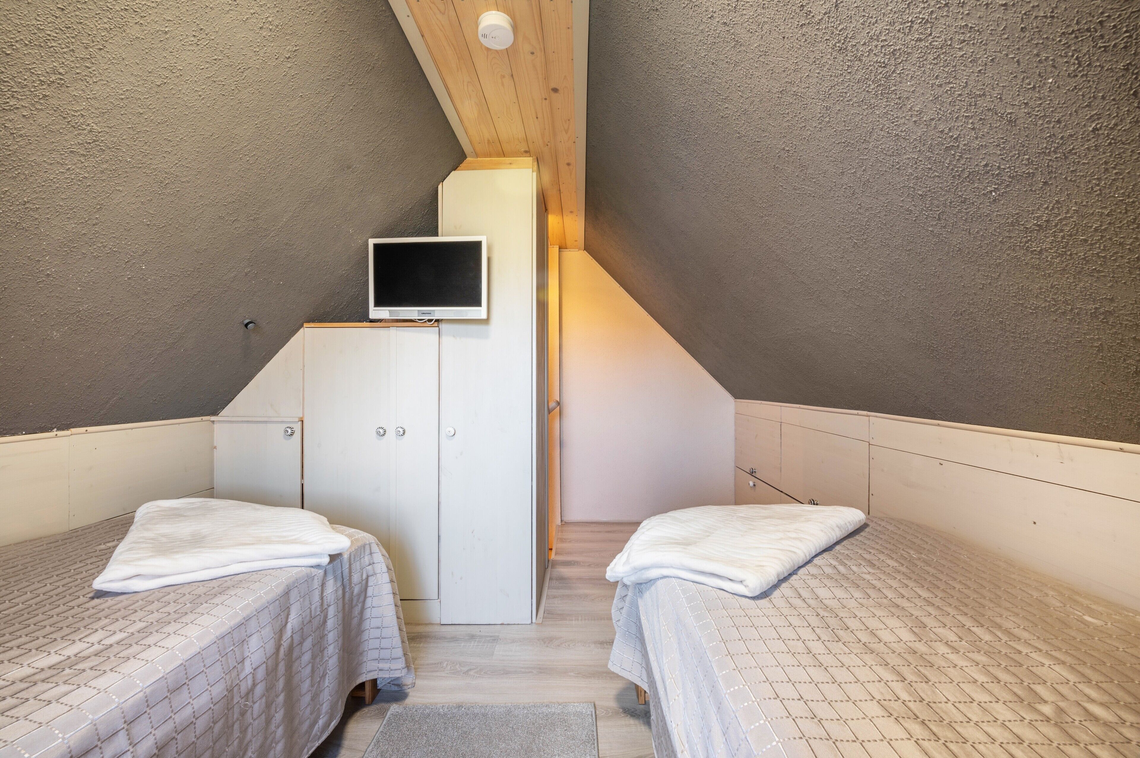 A small, single-room with two beds, a television, and a wardrobe.