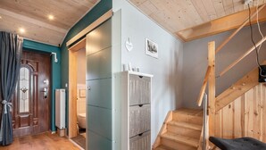 Une pièce avec un escalier en bois, un radiateur, une porte avec des rideaux et un petit banc.