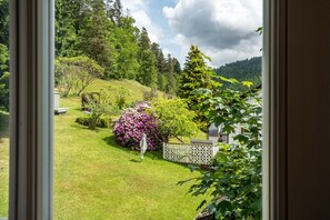 Vista di un rigoglioso giardino con diverse piante e alberi, un recinto bianco e una piccola costruzione sullo sfondo.