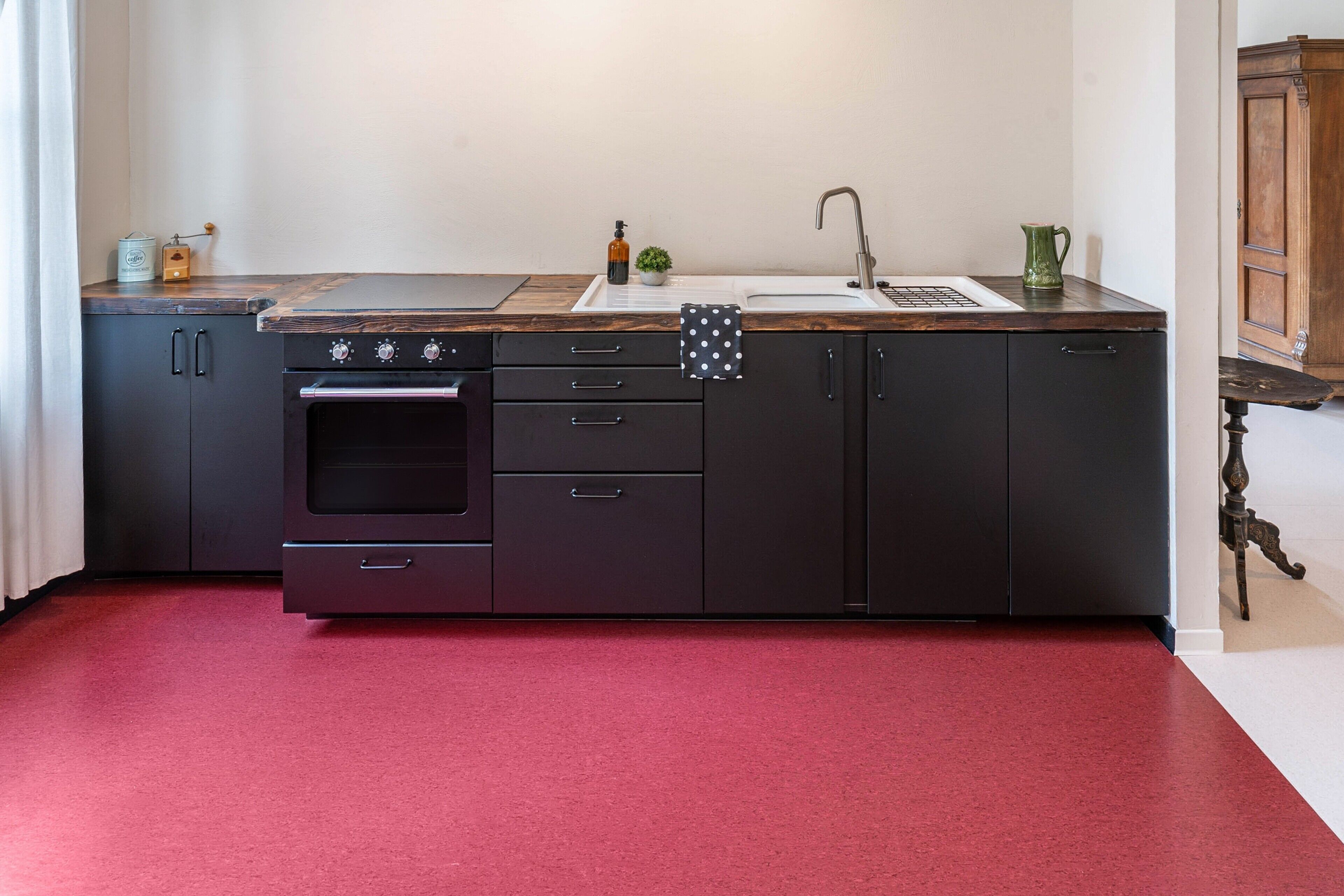 A kitchen with a red carpet, a sink, a stove, and cabinets.