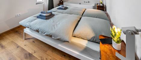Un lit simple avec un cadre en bois, une table de chevet avec une lampe et une fenêtre avec des rideaux.