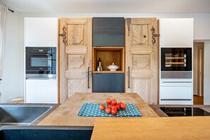 A kitchen with wooden cabinets, a built-in oven, a refrigerator, and a table with a polka dot placemat and tomatoes.